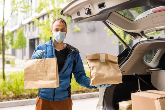 Postal delivery courier man wearing protective face mask in front of cargo van delivering package holding box due to Coronavirus disease or COVID-19.