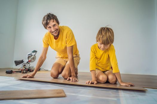 Father and son installing new wooden laminate flooring on a warm film floor. Infrared floor heating system under laminate floor.