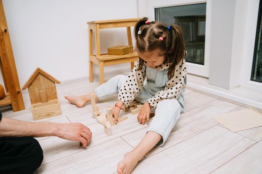 A little girl and her father build a tower out of wooden cubes. Playing with father. Happy Father's Day.