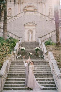 Bride and groom raising their hands up stand on stone steps. High quality photo