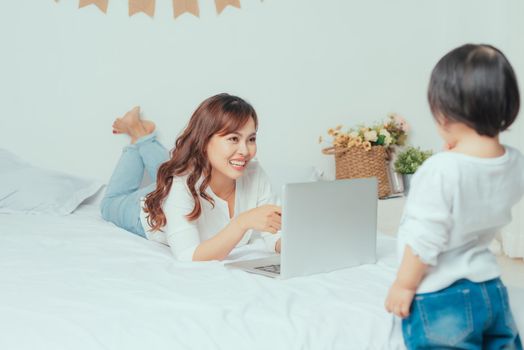Asian young woman is working busy on laptop while her daughter playing near mother