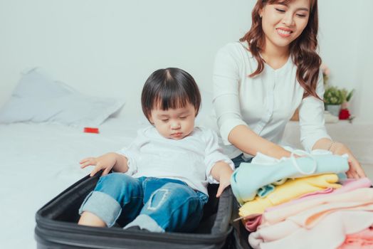 mother prepares clothes to put in her suitcase and her daughter plays with her suitcase