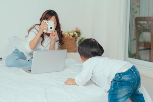 Image of young cheerful asian mother taking photo her baby on camera in cozy room