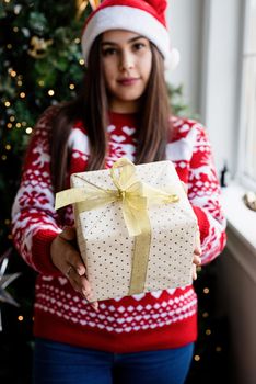 Packaging holiday gifts. Christmas gift wrapping. Young woman in red sweater holding christmas gifts