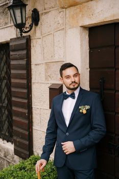 Groom in a suit stands near the door of an ancient building. High quality photo
