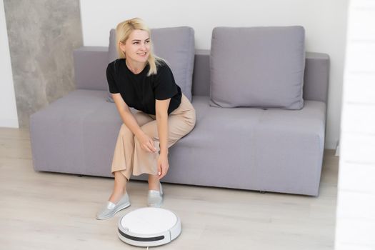 Modern life concept, woman relaxing, automatic robotic hoover clean the room while.
