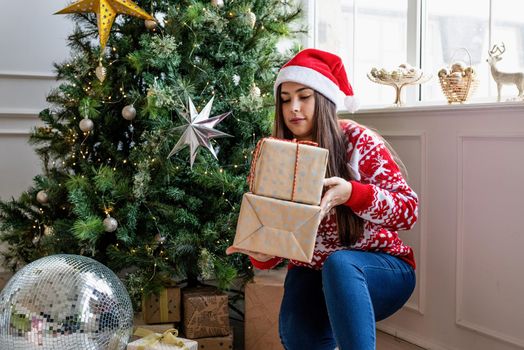 Packaging holiday gifts. Christmas gift wrapping. Young woman in red sweater holding christmas gifts