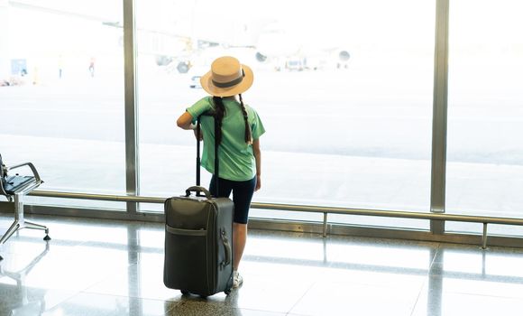 tourism, vacation, childhood and transportation concept - smiling little girl with travel bag, ticket and passport over airport background