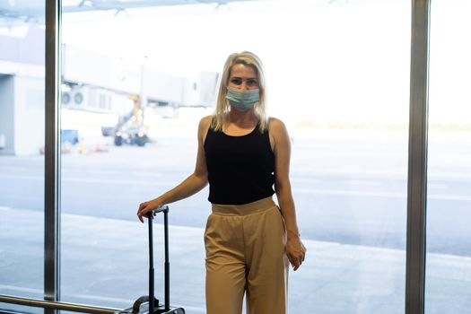 Caucasian traveler girl with medical face mask in airport. Woman wearing a protective mask against coronavirus. Facial hygienic mask for safety outdoor. Environmental awareness or virus spread fear
