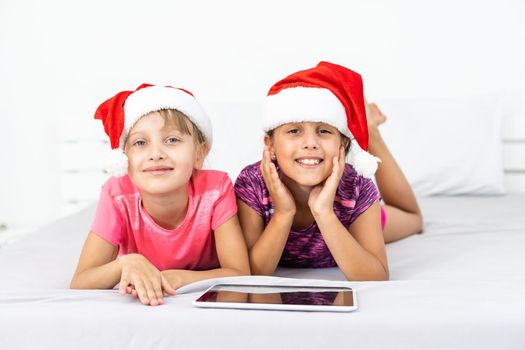 christmas, x-mas, winter, happiness concept - two adorable curly girls playing with tablet pc.