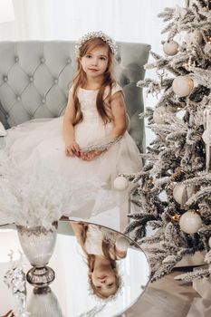 young caucasian girl with long fair hair and pretty face in white dress poses for the camera in christmas atmosphere and smiles