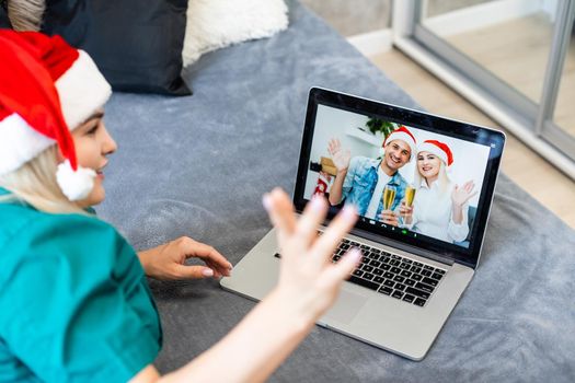 Smiling girl wearing Santa hat having video calling family by webcam. Woman with laptop sitting on kitchen at home using virtual meeting chat on holidays. Happy Christmas and New Year new normal