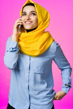 muslim woman in yellow hijab talking on the phone pink technology background. High quality photo