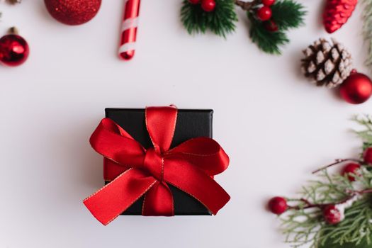 Christmas gift with a red bow on a white background with fir branches and decorations on a white background. View from above