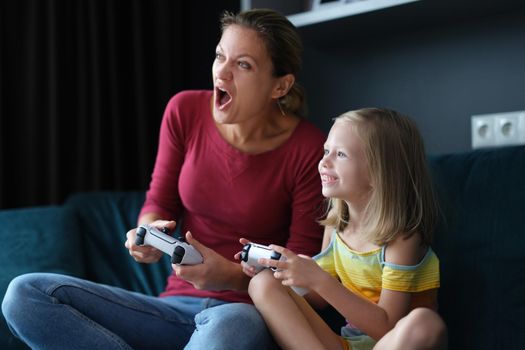 Mom and daughter are playing video games at home, close-up. Woman and child with game joysticks in hands