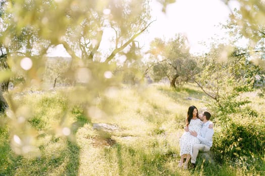 Man hugs the belly of a pregnant woman sitting on his lap in a park. High quality photo