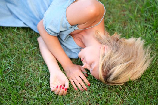 A young woman in a dress is sleeping on the green grass, close-up. Unity with nature, healthy ecology, relaxation