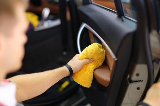 A man wipes a car door with a towel, close-up. Detailing, cleaning of leather surfaces of the vehicle interior