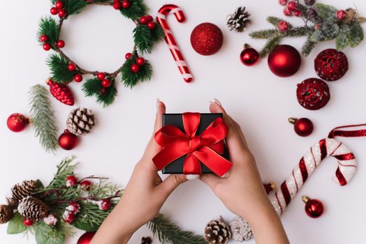 New Year or Christmas composition on a white background hands with a gift box, with a red ribbon with fir branches, toys, copy space for congratulations. Give a gift.