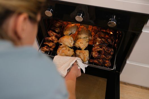 The woman determines the readiness of the chicken in the oven, close-up, blurry. BBQ cooking, grill wings