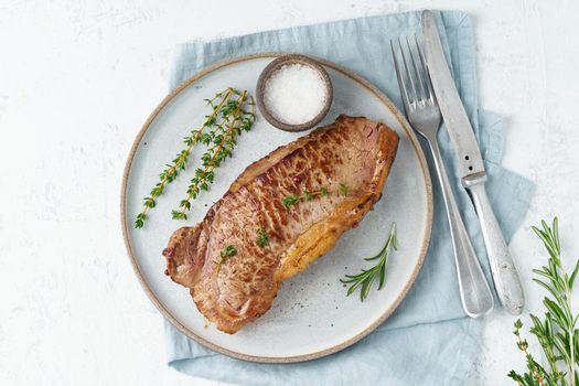 Keto ketogenic diet beef steak, striploin on gray plate on white background. Paleo food recipe with whole big piece of meat and a seasoning. Copy space, top view