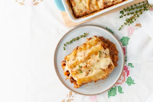 Cannelloni pasta with filling of ground beef, tomatoes, baked with bechamel tomato sauce and a mozzarella. Classical Italian cuisine, white tablecloth with embroidery, rustic style, top view, copy space