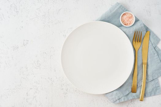 Clean empty white plate, fork and knife on white stone table, copy space, mock up, top view. Concept for menu with utensil