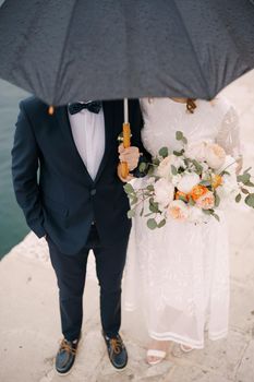 Bride and groom stand on the pier under an umbrella. Close-up. High quality photo
