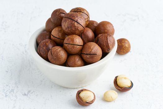 Plate with almonds in endocarp, whole and chopped open nuts in bulk on cutting board with knife on a white background, side view.