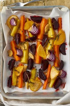 Colorful roasted vegetables on tray with parchment. Mix of carrots, beets, turnips, rutabaga, onions. Vegetarianism, veganism, proper nutrition, lchf. Top view, vertical