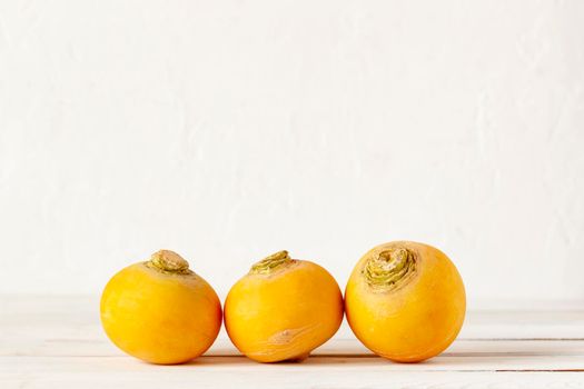 three yellow raw organic turnips on the wooden background, copy space