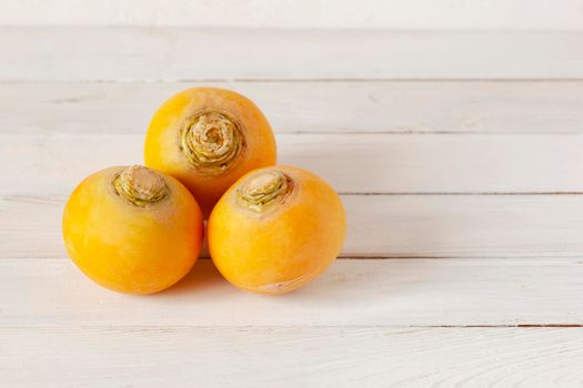 three yellow organic raw turnips in a form of triangle on white wooden background, copy space