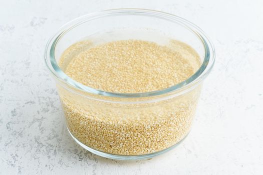 Soaking quinoa cereal in water to ferment cereals and neutralize phytic acid. Large glass bowl with grains flooded with water. Side view, close up, white background