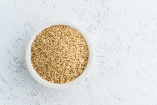 Brown rice in a white bowl on white background. Dried cereals in cup, vegan food, fodmap diet. Top view, close up.