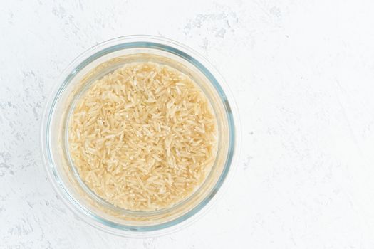 Soaking brown rice cereal in a water to ferment cereals and neutralize phytic acid. Large glass bowl with grains flooded with water. Top view, close up, white background