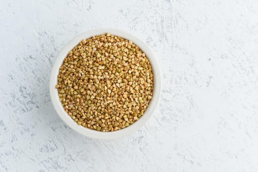 Green buckwheat in a white bowl on white background. Dried cereals in cup, vegan food, fodmap diet. Top view, close up.