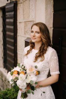 Bride with a bouquet leans on the wall at the door of an old stone house. High quality photo