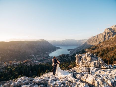 Bride and groom stand hugging each other on the top of the mountain and look at the valley. High quality photo