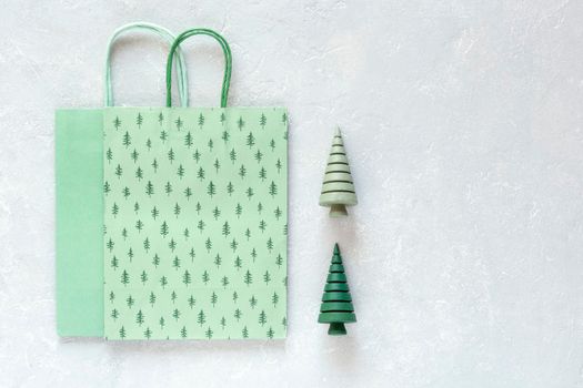 green paper Christmas tree pattern bags and wooden Christmas trees on grey background, top view, copy space