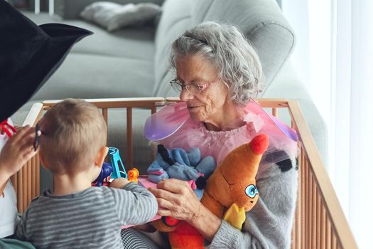 Gray-haired grandmother plays with her little grandchildren in a flat