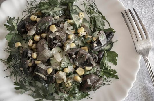 On the table on a plate is an appetizing salad of mushrooms, onions, canned corn and cucumbers. Top view, close-up