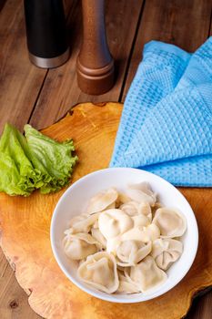 Dumplings in a white plate with salad on a wooden background. Russian national food.