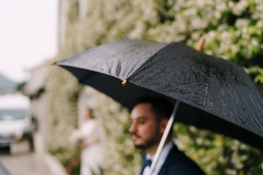 Raindrops on an umbrella over the groom near the building. Blur. Close-up. High quality photo