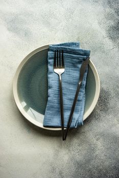 Ceramic plates, same color cutlery with stripped napkin served on grey concrete background