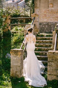 Bride in a white mermaid dress climbs the steps to the old chapel. High quality photo