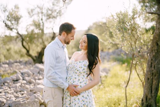 Man hugging a pregnant woman while standing by the stones in the park. High quality photo