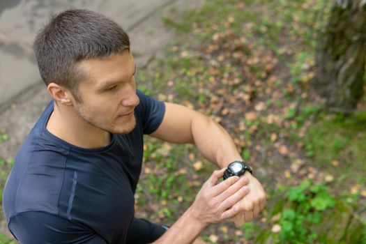 A man looks at the clock time in the park outdoors, around the forest, oaks green grass young enduring athletic athlete. active sport forest, workout trail training legs motion, park Summer body feet stretches