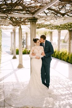 Groom kisses bride standing by the column in the old courtyard. High quality photo