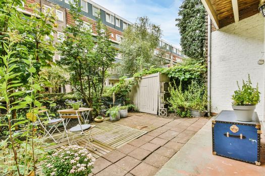 Green backyard of a house with wooden table and chairs and blue chest
