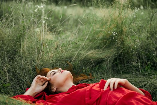 pretty woman in red dress lies on the grass freedom landscape. High quality photo